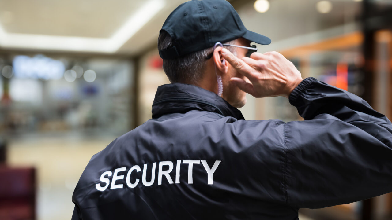Security Guard Listening To Earpiece Against Building